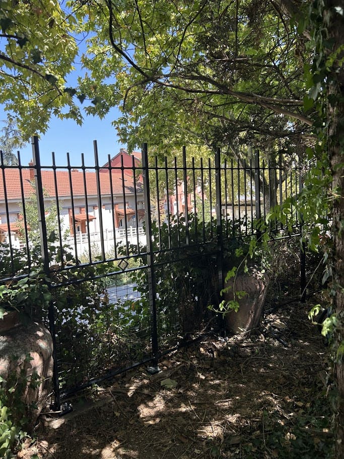 Fabrication et pose d'une clôture barreaudée en fer forgé. la clôture est posée en surplomb du cours Emile Zola à Villeurbanne. Elle a une hauteur de 2 mètres et elle est constituée de 13 sections d'un mètre de long. La partie haute est barreaudée verticalement en fer plat de sections rectangulaire et carré. La partie basse est remplie en grillage de maille 100x50. la séparation entre les deux est marqué par des carrés façonnés type art déco. Elle vient en remplacement d'un garde corps type art déco d'un mètre de haut. Un élément sur trois est constitué uniquement de la partie supérieure afin d'enjamber d'énormes pots ou pousse du lierre. La végétalisation à été préservée au maximum. L'ensemble est peint en ral 9005 noir. Clôture barreaudée métallique réalisée et installée par l'entreprise Claude Jeandin métallerie.