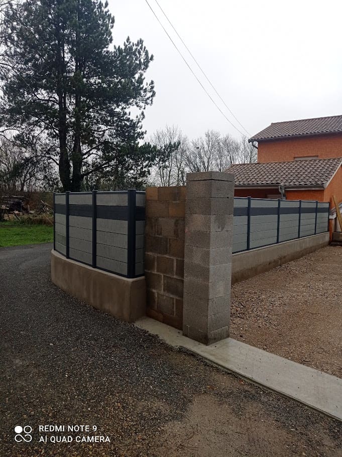 Pose d'un portillon et d'une clôture sur muret en composite de la marque Océwood. Les poteaux sont en aluminium ral 7016 et le remplissage composé de cinq rangées de lames décoratives horizontales teintes Basalte et d'une rangée intercalée de lames en teinte Graphite. La hauteur totale est de 180 cm. Portillon et clôture Océwood installés par l'entreprise Claude Jeandin métallerie.
