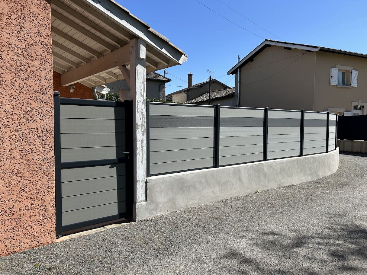 Pose d'un portillon et d'une clôture sur muret en composite de la marque Océwood. Les poteaux sont en aluminium ral 7016 et le remplissage composé de cinq rangées de lames décoratives horizontales teintes Basalte et d'une rangée intercalée de lames en teinte Graphite. La hauteur totale est de 180 cm. Portillon et clôture Océwood installés par l'entreprise Claude Jeandin métallerie.
