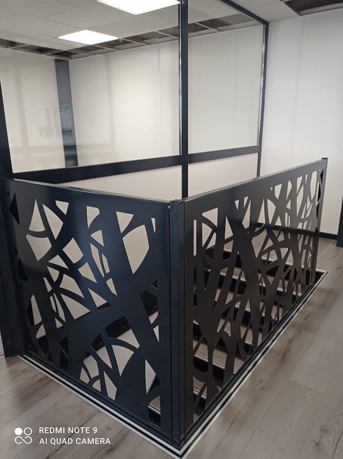 Fabrication et pose d'un garde-corps en tôles découpe laser sur un palier de bureaux. Les deux panneaux sont tôlés et découpés au laser de motifs géométriques. Les fixations sont entièrement cachées. L'ensemble est peint en ral 7016 gris. Garde-corps réalisé et installé par l'entreprise Claude Jeandin métallerie.