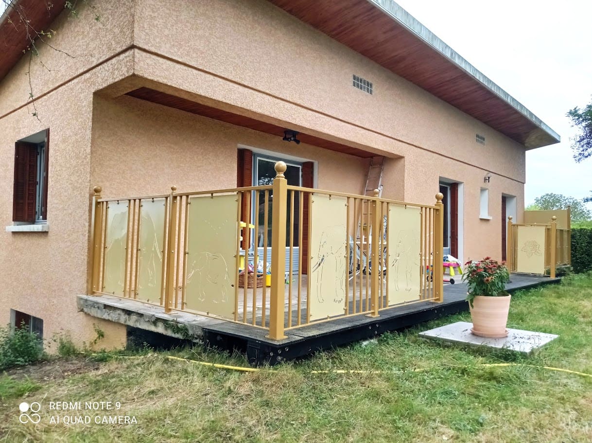 Garde-corps acier sur terrasse en tôles découpe laser et barreaudages. Les poteaux de section rectangulaires sont ornés d'une boule décorative en fer forgé. Le remplissage est constitué de panneaux barreaudés verticalement entrecoupés de tôles en découpe laser. Les motifs sur les tôles représente la marche d'une harde d'éléphants sur une partie de la terrasse. Sur l'autre partie se sont des motifs floraux. L'ensemble est bicolore, ral 1011 pour les poteaux et les cadres barreaudés, ral 1001 pour les tôles. Garde-corps réalisés et installés par l'entreprise Claude Jeandin métallerie.