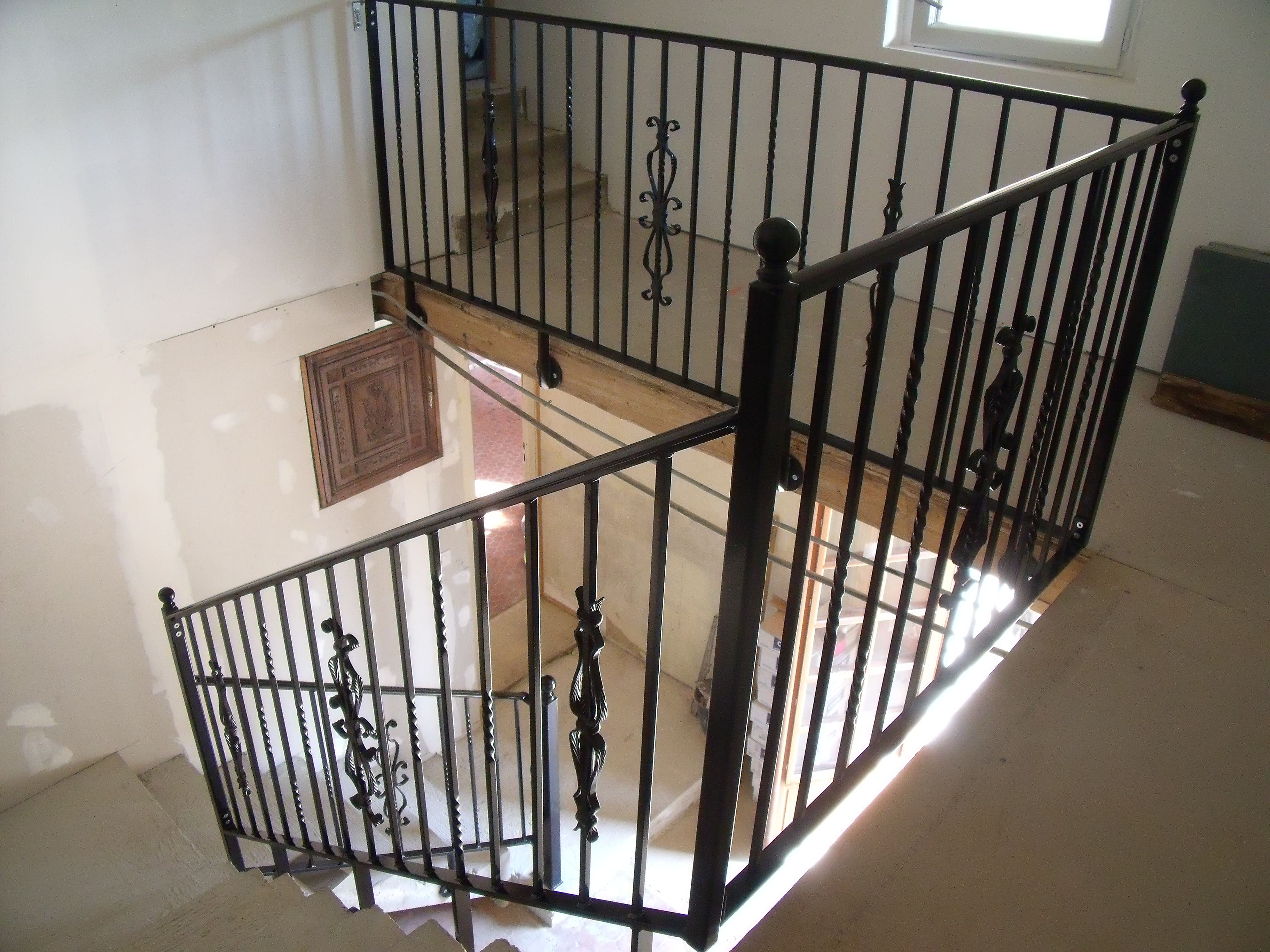 Fabrication et pose d'un garde-corps en fer forgé sur un escalier intérieur. Le barreaudage est verticale, il comprend des barreaux simples en carré de 14, des barreaux torsadés et différents éléments décoratifs forgés. Les poteaux d'angle sont ornés d'une boule décorative, la main courante est moulurée. L'ensemble est peint en ral 9005. Garde-corps réalisé par l'entreprise Claude Jeandin métallerie.