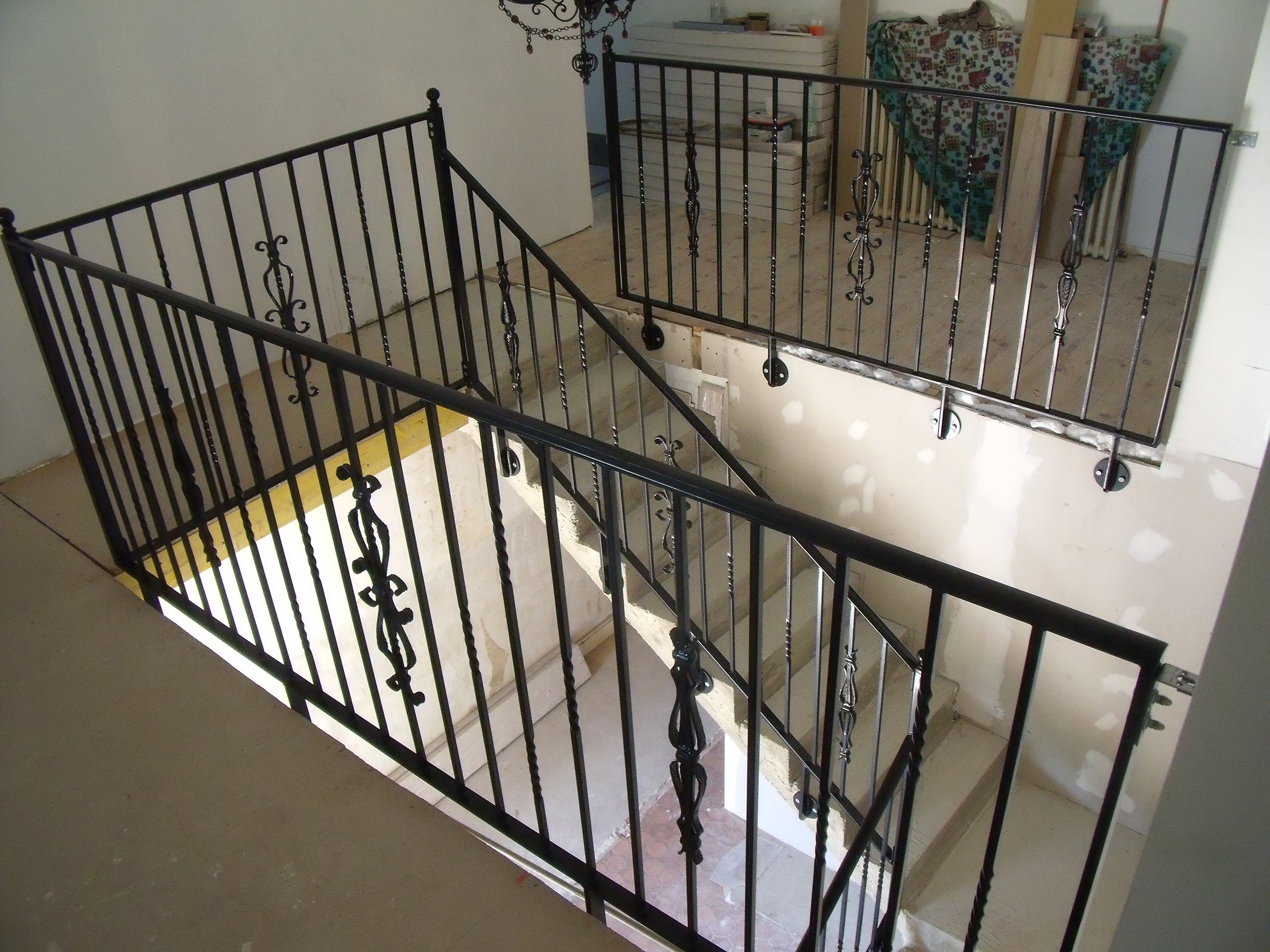 Fabrication et pose d'un garde-corps en fer forgé sur un escalier intérieur. Le barreaudage est verticale, il comprend des barreaux simples en carré de 14, des barreaux torsadés et différents éléments décoratifs forgés. Les poteaux d'angle sont ornés d'une boule décorative, la main courante est moulurée. L'ensemble est peint en ral 9005. Garde-corps réalisé par l'entreprise Claude Jeandin métallerie.