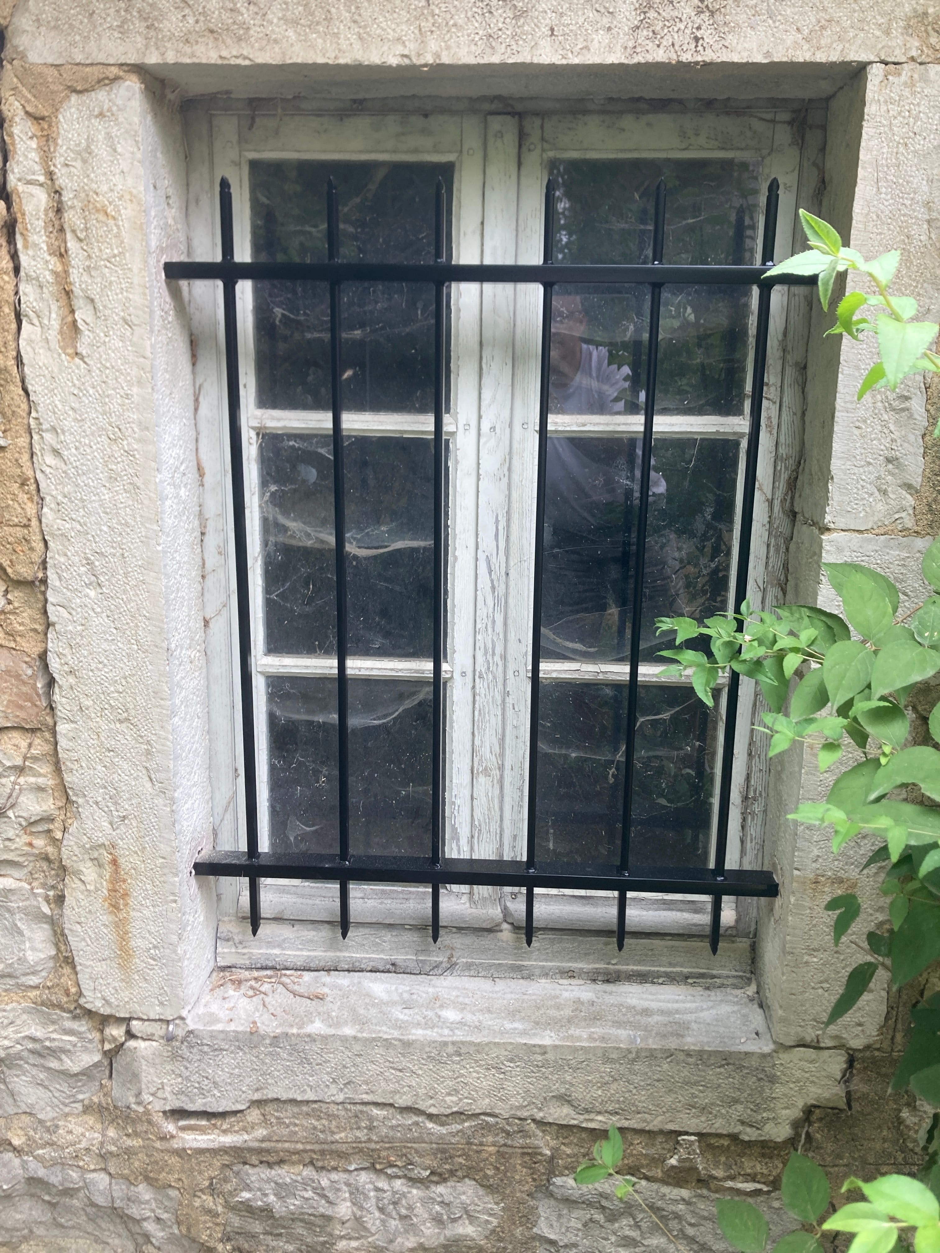 Fabrication et pose de grille de défense en fer forgé sur une ancienne école catholique des années 1900 transformée en habitation. le barreaudage est verticale, l'extrémité de chaque barreaux est en forme de goutte d'eau façonnée à la main. Les grilles sont scellées dans les encadrements des fenêtres. Le lot de 8 grilles a été fabriqué identique aux grilles existantes. L'ensemble est peint en ral 9005 noir et s'intègre parfaitement au bâtiment. Grilles de défense métallique réalisées et installées par l'entreprise Claude Jeandin métallerie.