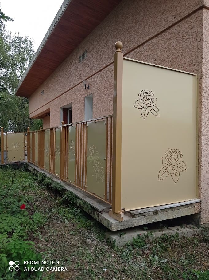 Brise vue acier sur terrasse en tôles découpe laser. Fixé en bout de terrasse entre le mur de la maison et un poteaux en tube carré. Le remplissage est composé d'une tôle décorées de motifs florales en découpe laser. Il est installé au bout de la terrasse en fermeture d'un garde-corps métallique. L'ensemble est bicolore, ral 1011 pour le poteau et ral 1001 pour la tôle. Brise vue réalisé et installé par l'entreprise Claude Jeandin métallerie.