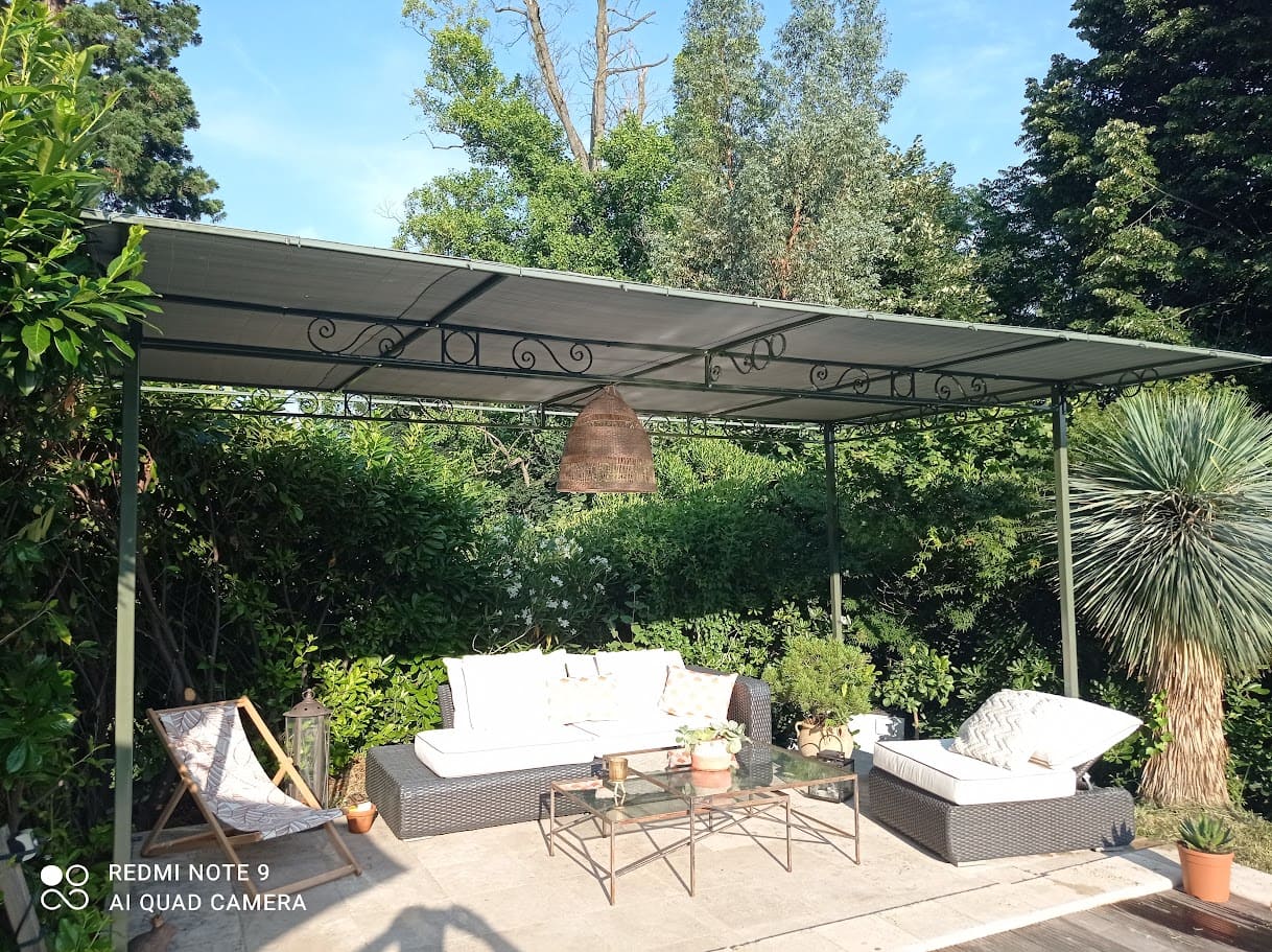 Fabrication et pose d'une pergola métallique en fer forgé. Les quatre poteaux sont de section carré, les échelles sont ornées de volute forgées, les traverses supportent une toile d'ombrage. La hauteur de passage est de 2 mètre 50. Elle protège agréablement tout l'été un espace de détente au bord d'une piscine. L'ensemble est peint en ral 7009. Pergola réalisée et installée par l'entreprise Claude Jeandin métallerie.