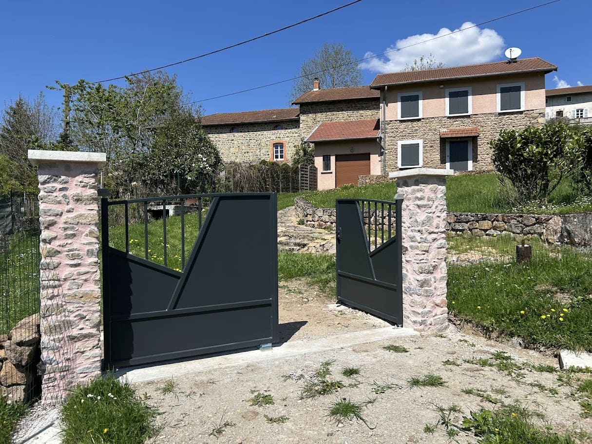 Fabrication et pose d'un portail métallique personnalisé à deux vantaux. L'ossature est tubulaire, la traverse supérieure est cintrée. Le remplissage est constitué sur chaque vantail d'une tôle rectangulaire en partie basse, de deux tôles à pans coupés et d'un espace barreaudé verticalement en partie haute. L'ensemble est peint en ral 9005. L'ouverture est manuelle, il est équipé d'une serrure décorative de marque LOCINOX. Il est fixé sur deux piliers en pierres maçonné. Portail réalisés par l'entreprise Claude Jeandin métallerie.