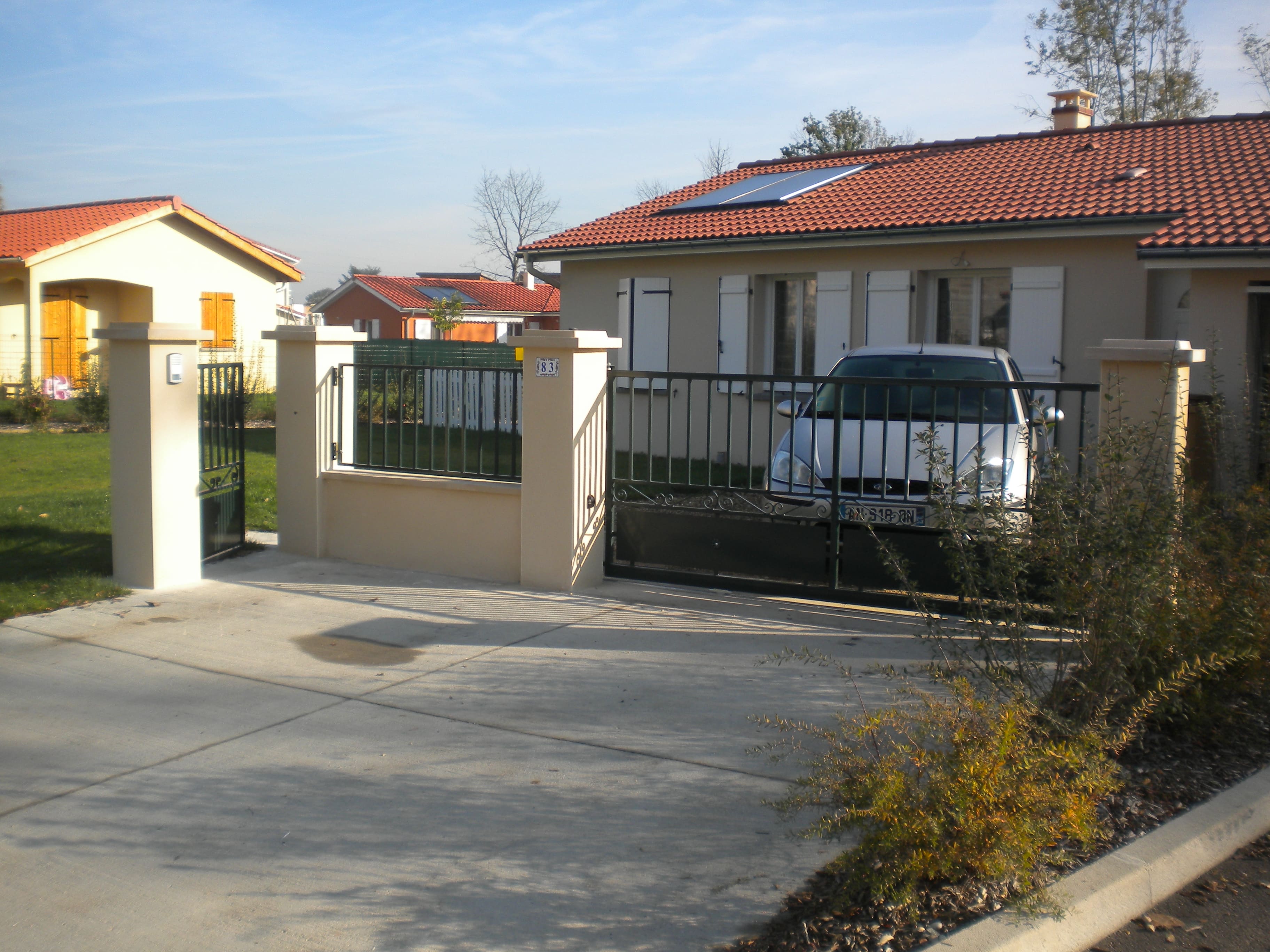 Fabrication et pose d'un ensemble portillon, clôture et portail en fer forgé. La partie supérieure est barreaudée, la partie basse est constituée d'une tôle pliée en pointe de diamant. L'espace entre les deux est décoré de volutes en fer forgé. L'ensemble est peint en ral 9005. Portail, portillon et clôture réalisés par l'entreprise Claude Jeandin métallerie.