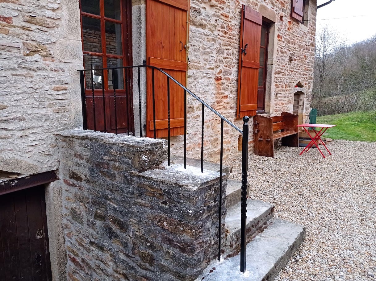Fabrication et pose d'une rampe en fer forgé sur un escalier extérieur. Le barreaudage et verticale, il est composé de barreaux simples et de barreaux torsadés en carré de section de 14 mm. Le poteau de tête en carré de 30 mm est orné d'une boule décorative, la main courante est moulurée. L'ensemble est peint en ral 9005. Rambarde réalisé par l'entreprise Claude Jeandin métallerie.