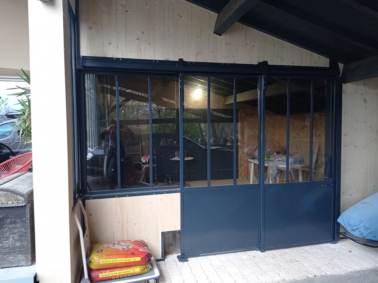 Fabrication et pose d'une verrière métallique comprenant un châssis fixe et une double porte coulissante pour fermer un atelier. La partie haute et vitrée, la partie basse et remplie par une tôle pliée en pointe de diamant. L'ensemble et peint en ral 7016. Verrière réalisée par l'entreprise Claude Jeandin métallerie.